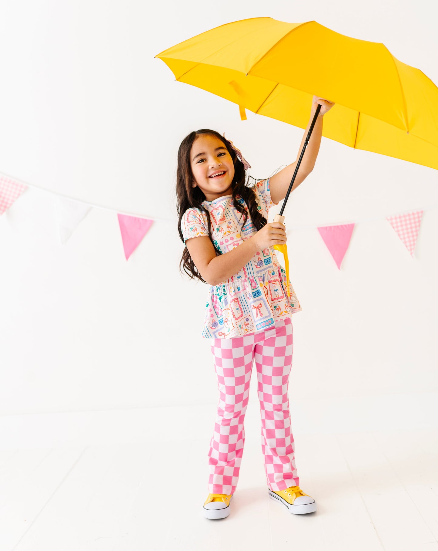Child holding a yellow umbrella against a white background with pink flags