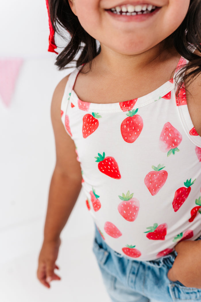 Child wearing a white tank top with red strawberry pattern on a plain background