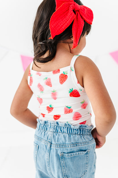 Child wearing a strawberry-patterned tank top and red headband on a white background