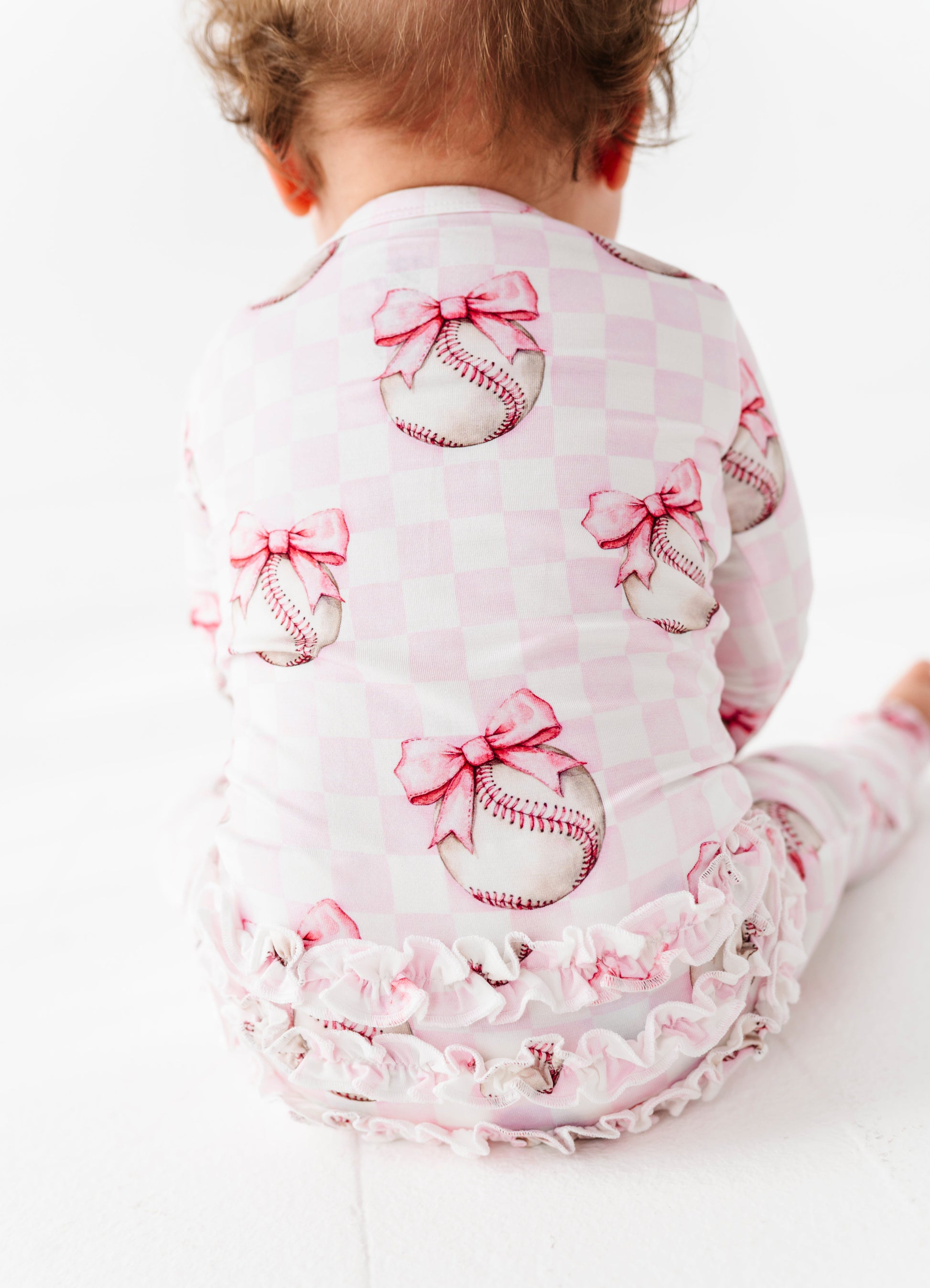 Baby wearing a pink bamboo zip romper with baseball and bow designs on a white background