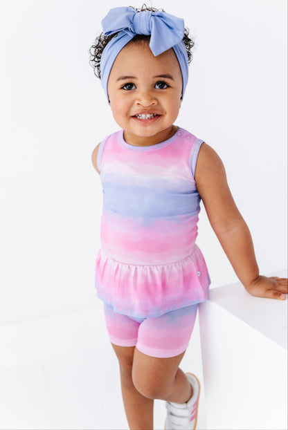 Baby wearing a colorful tie-dye bamboo-cotton peplum top and matching shorts, with a purple headband on a white background