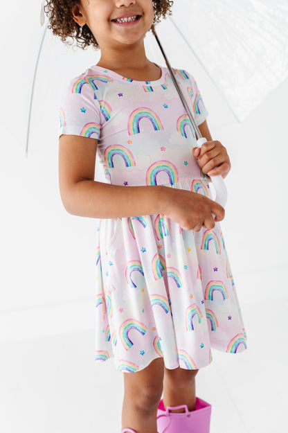 Child wearing a bamboo dress with watercolor rainbow patterns holding a transparent umbrella.