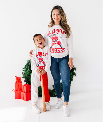 A woman and a young boy wearing matching white Christmas sweaters with a red and white 'Eaghting' graphic, standing in front of a white studio background with a small green tree and red gift boxes.