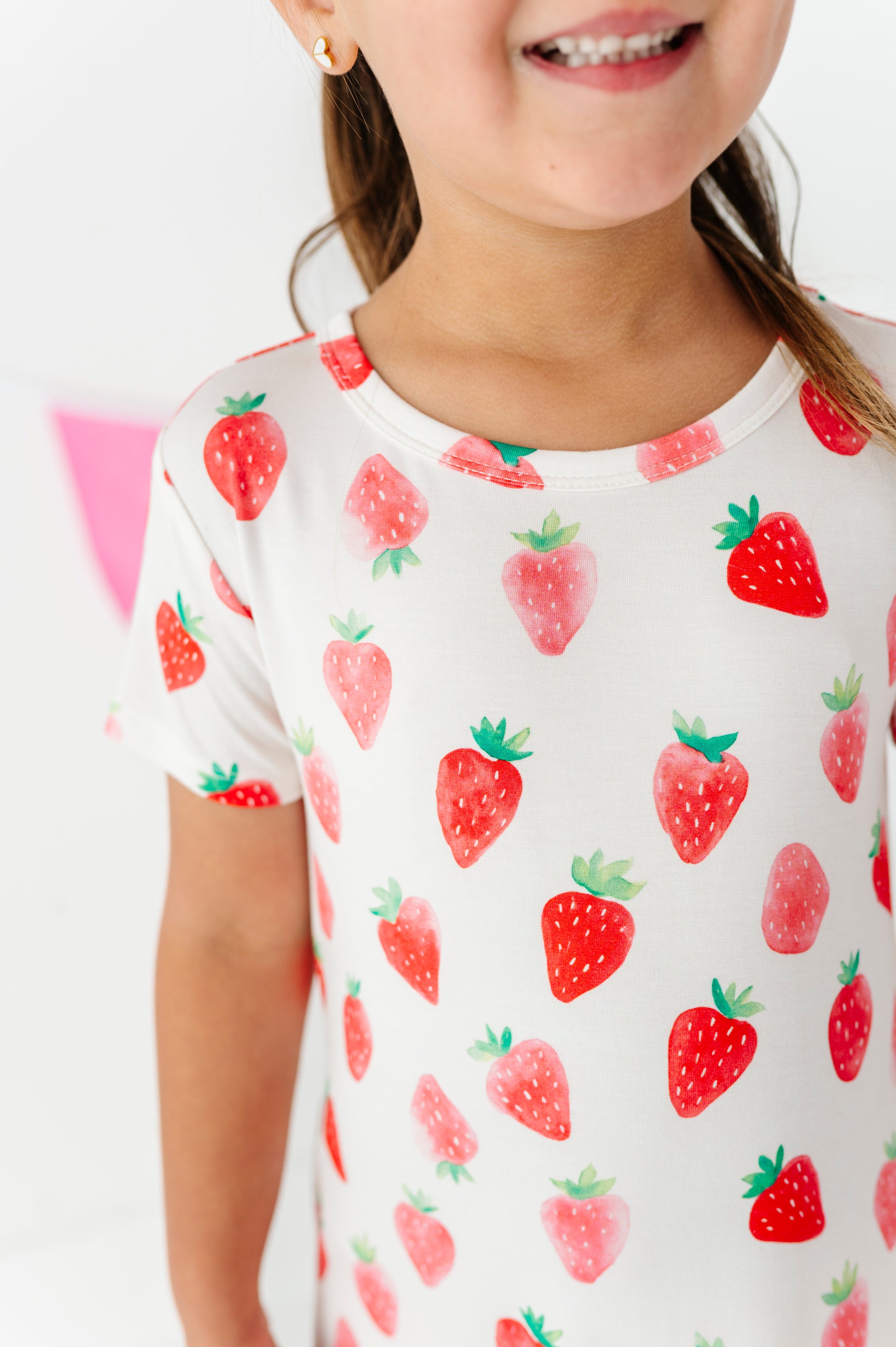 Child wearing a white dress with red strawberry pattern on a plain background