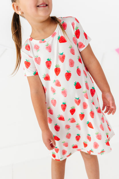 Child wearing a white dress with red strawberry pattern on a white background