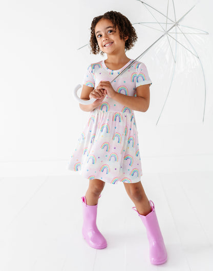 Child wearing a bamboo dress with watercolor rainbows and holding a transparent umbrella on a white background