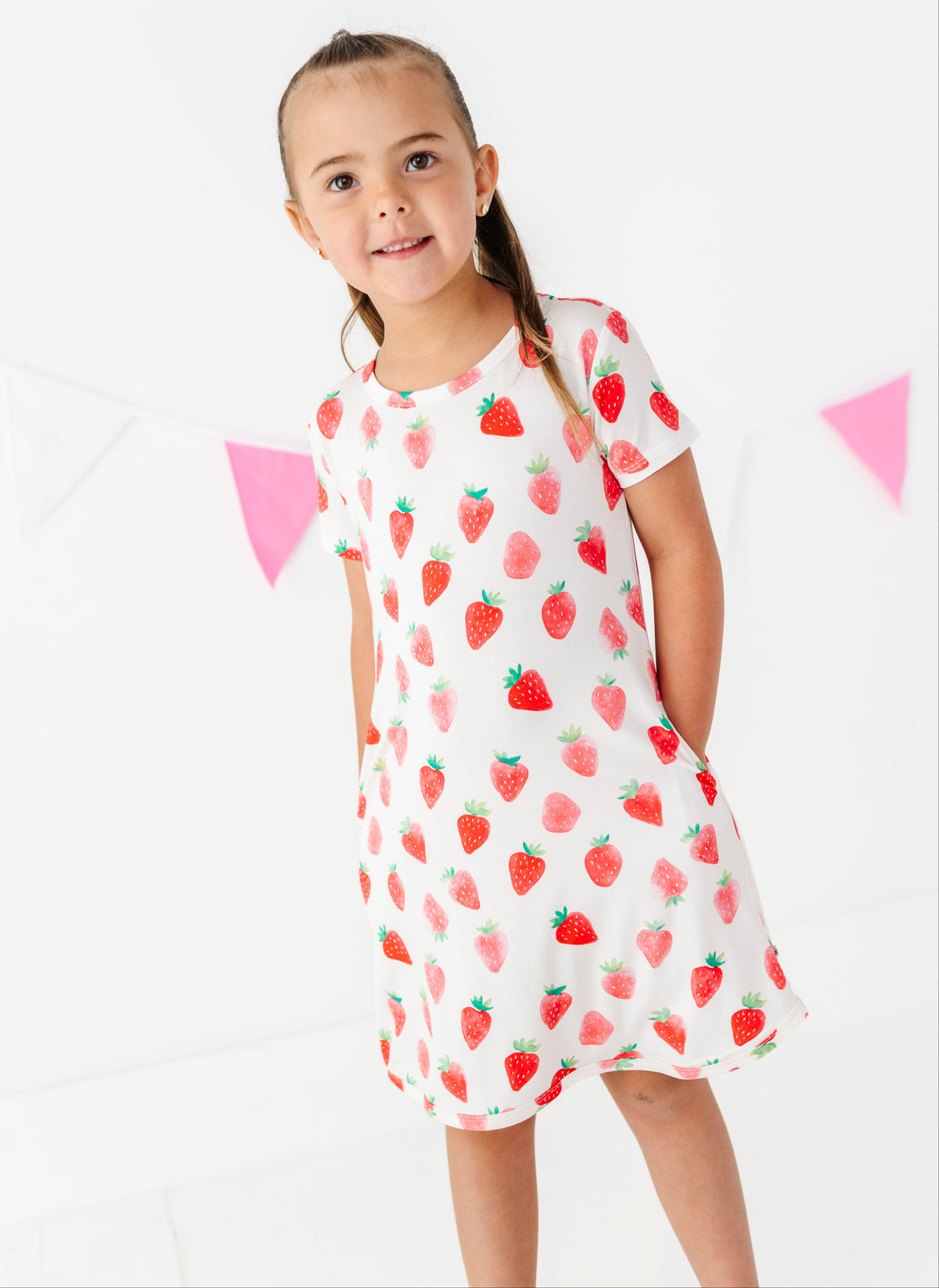 Young girl wearing a strawberry patterned dress on a white background
