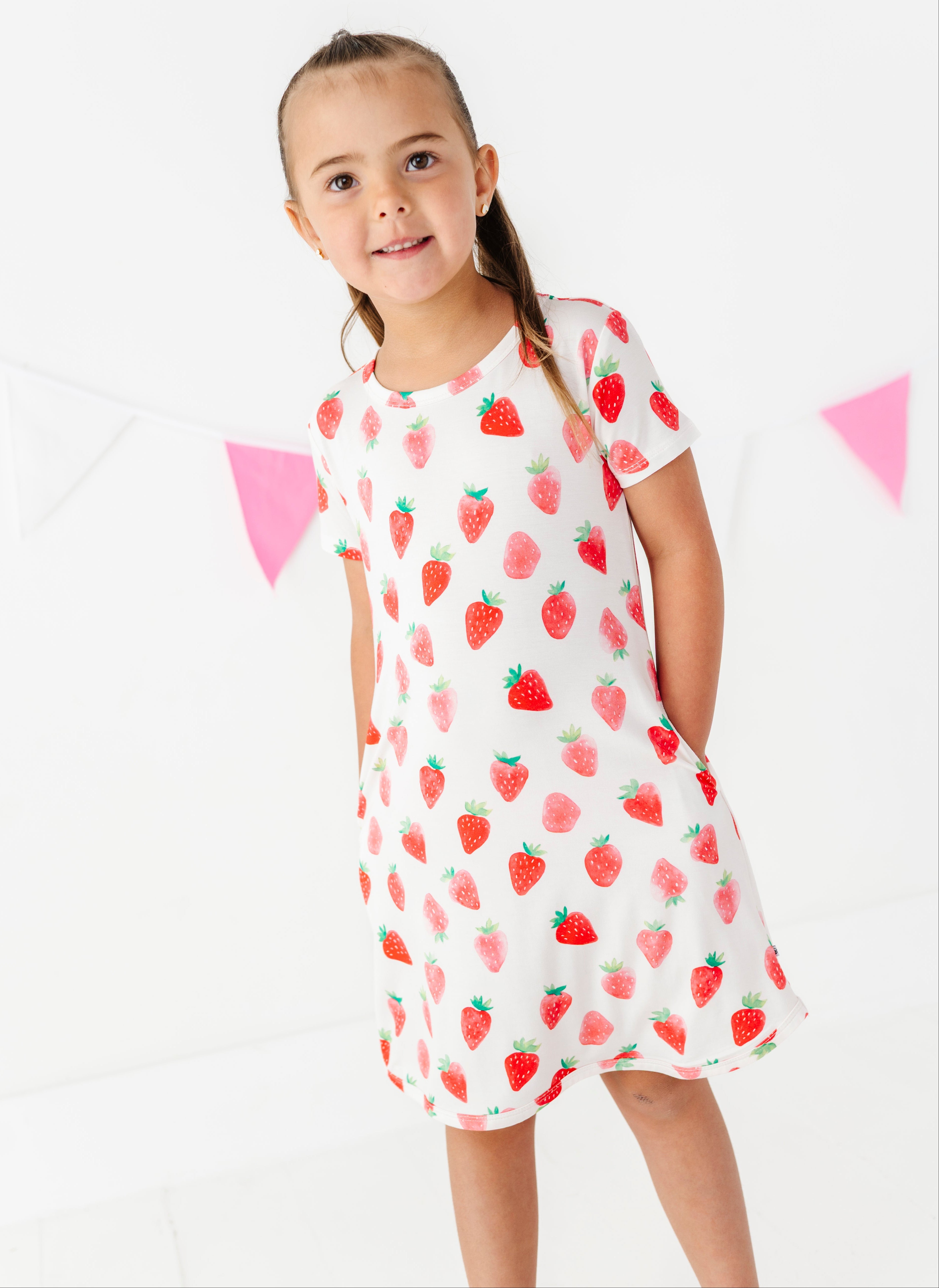 Young girl wearing a strawberry patterned dress on a white background