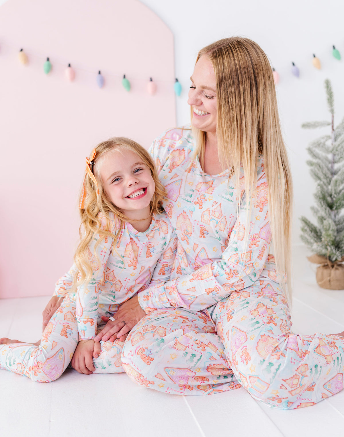 A mom and daughter cuddling while wearing matching bamboo pajamas featuring gingerbread villages 