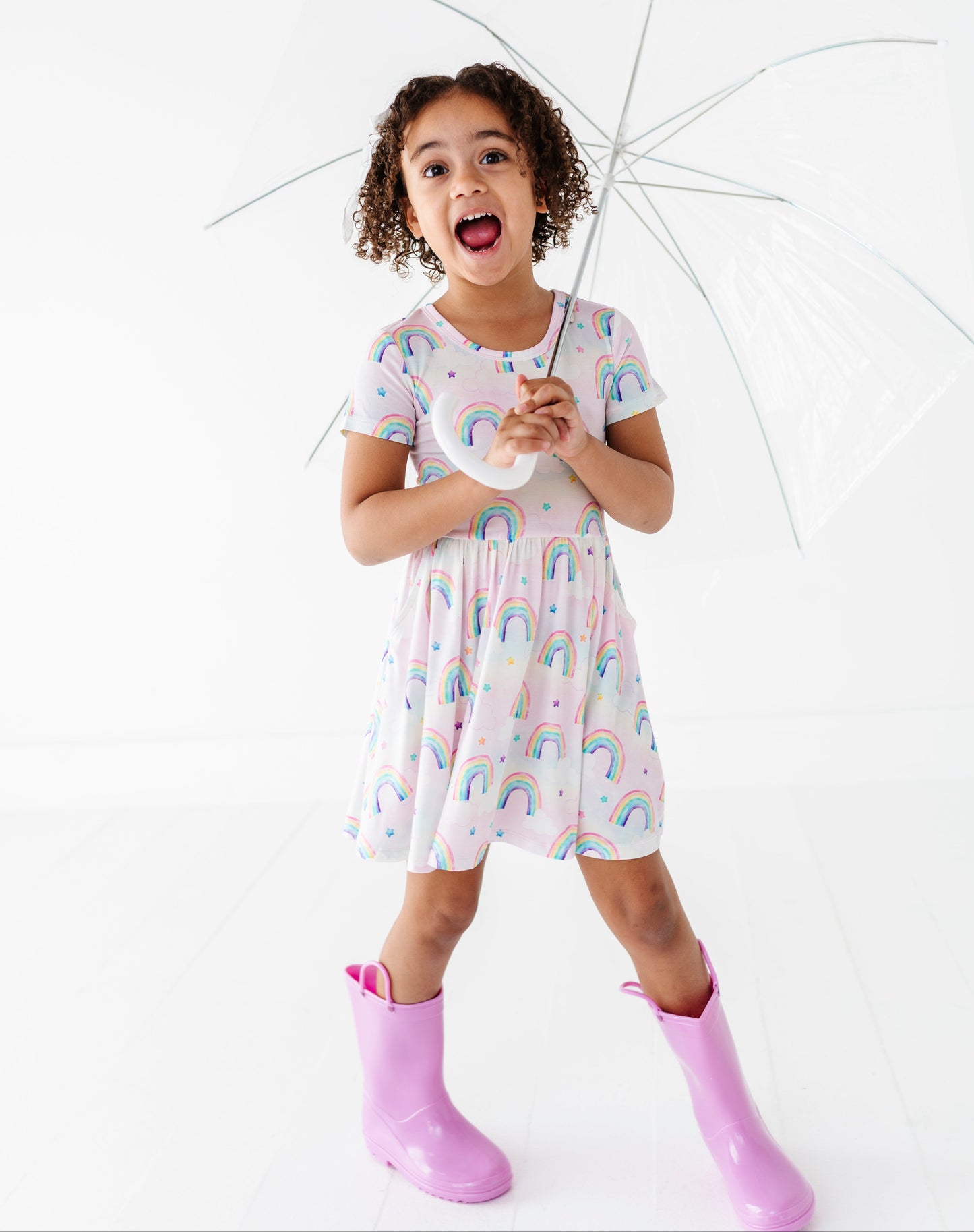 Child wearing a bamboo dress with watercolor rainbows and holding an umbrella on a white background