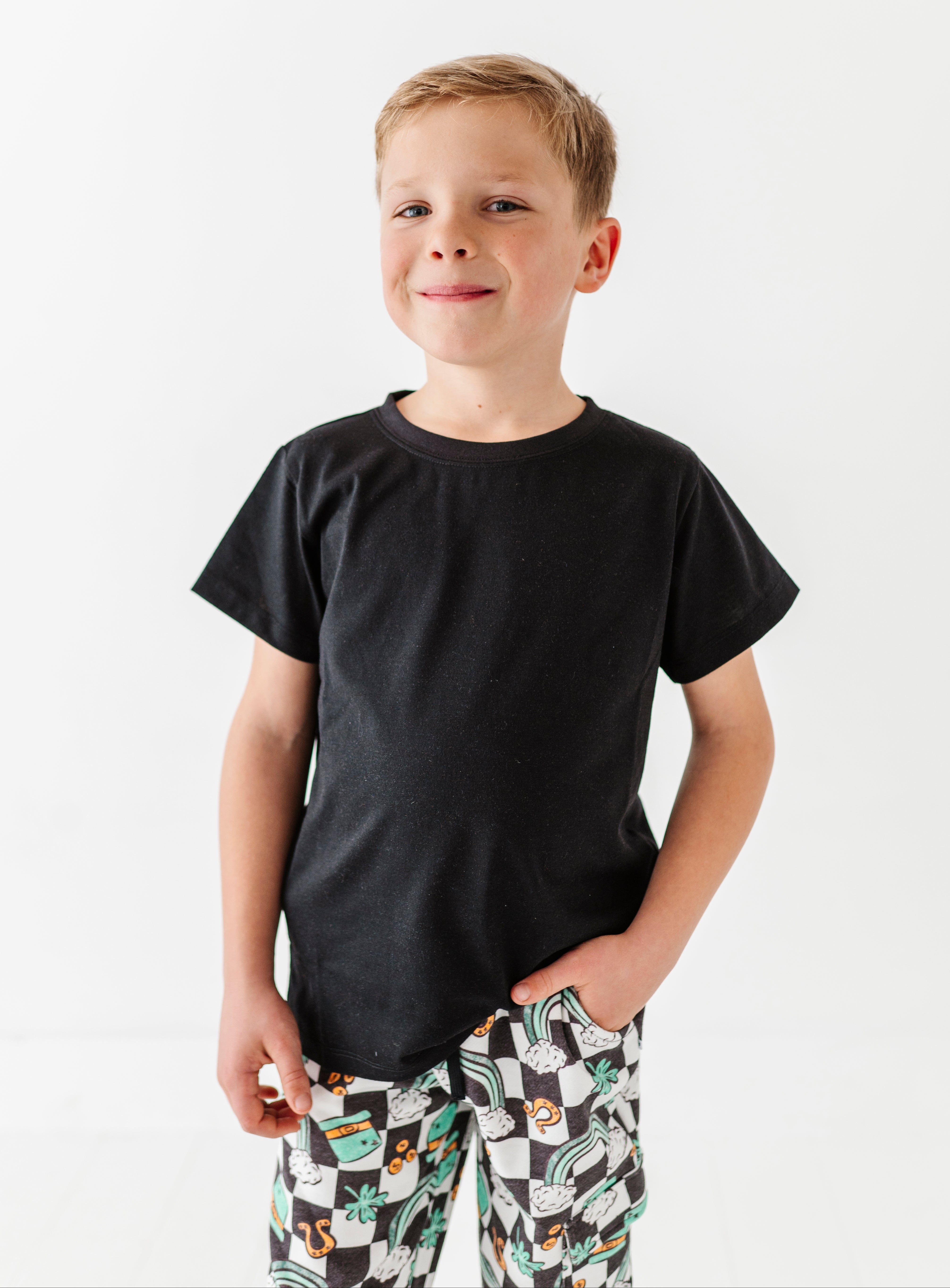 Young boy wearing a black t-shirt and patterned pants on a white background