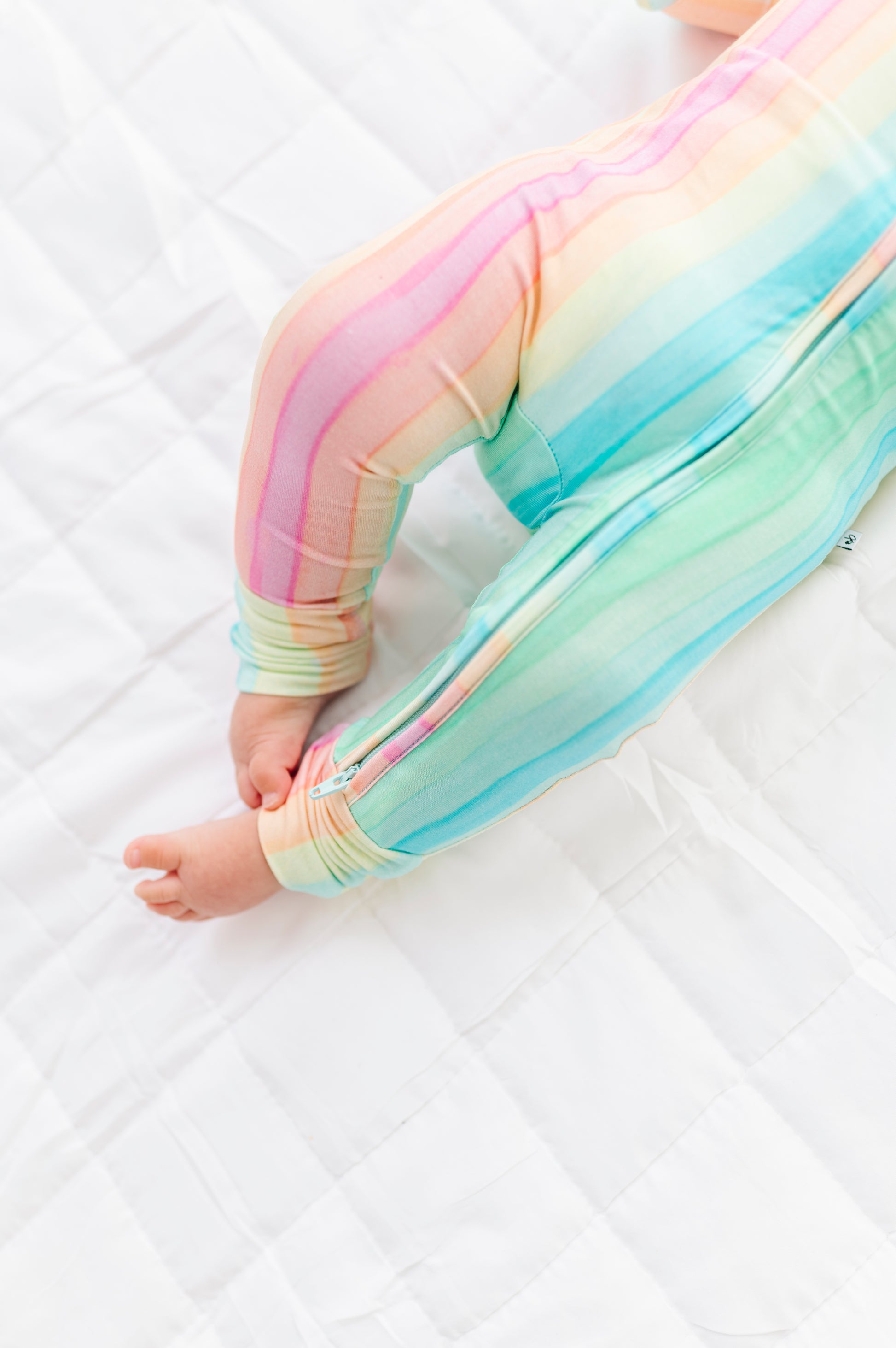 Close up of pastel rainbow stripe bamboo romper showing smooth zipper and soft fabric texture