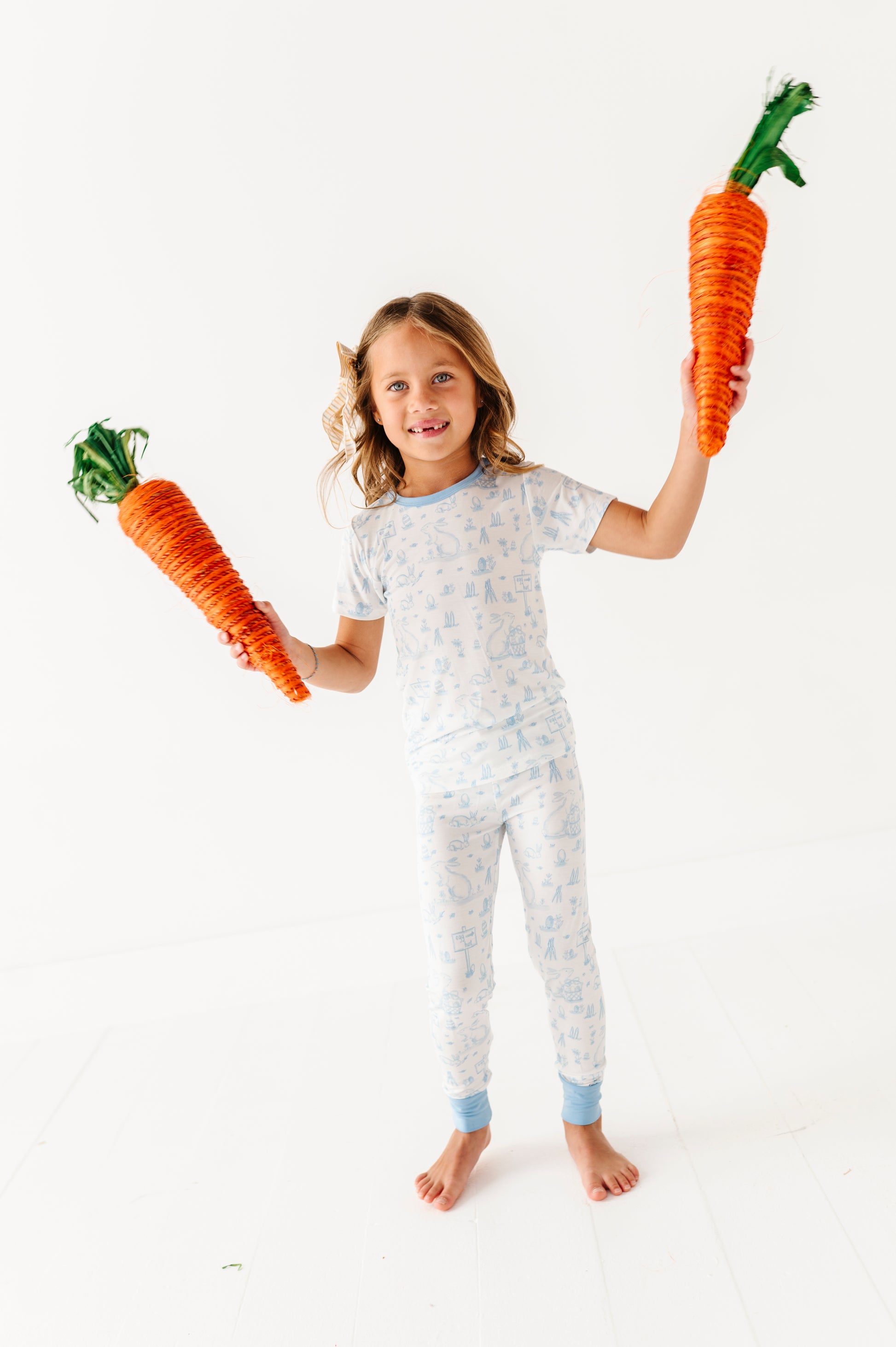 Child wearing Easter bamboo pajamas holding two large carrot toys against a white background