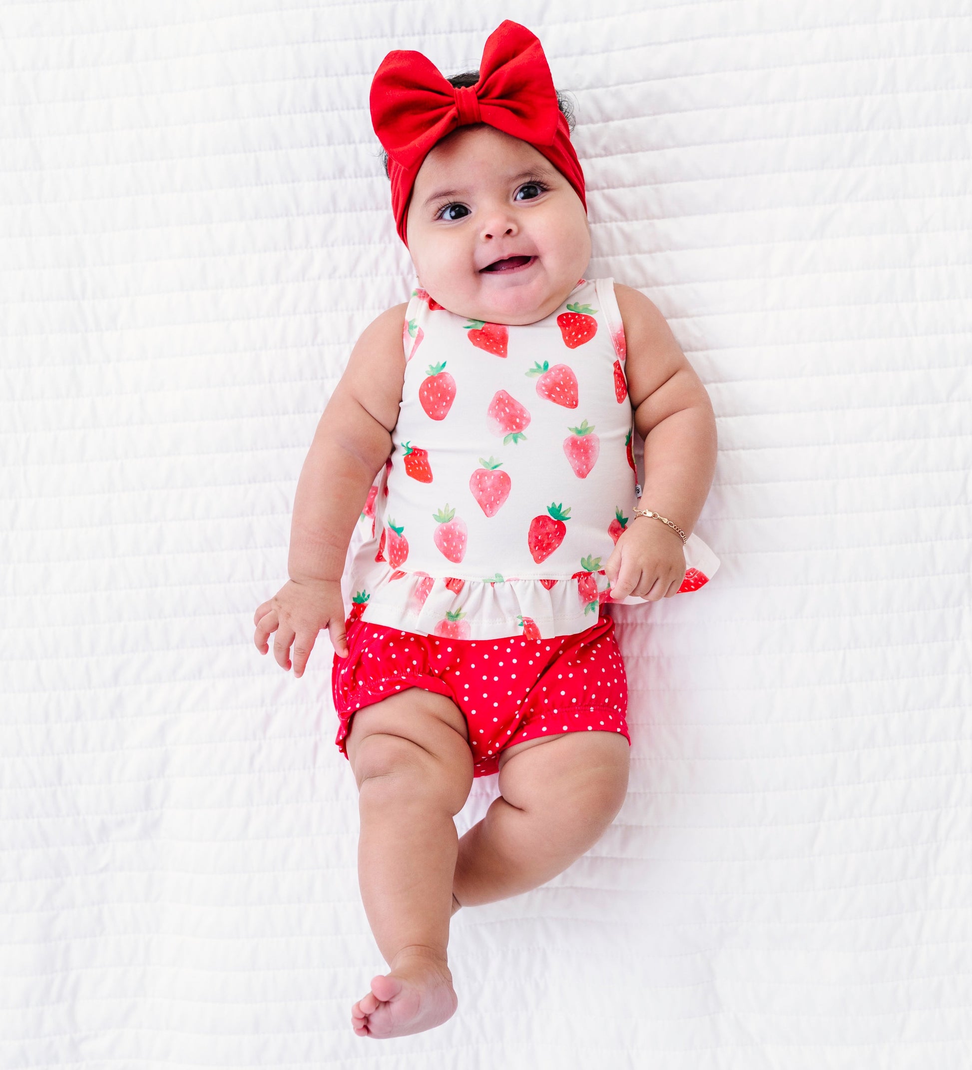 Baby wearing a strawberry print outfit with a red bow on a white background
