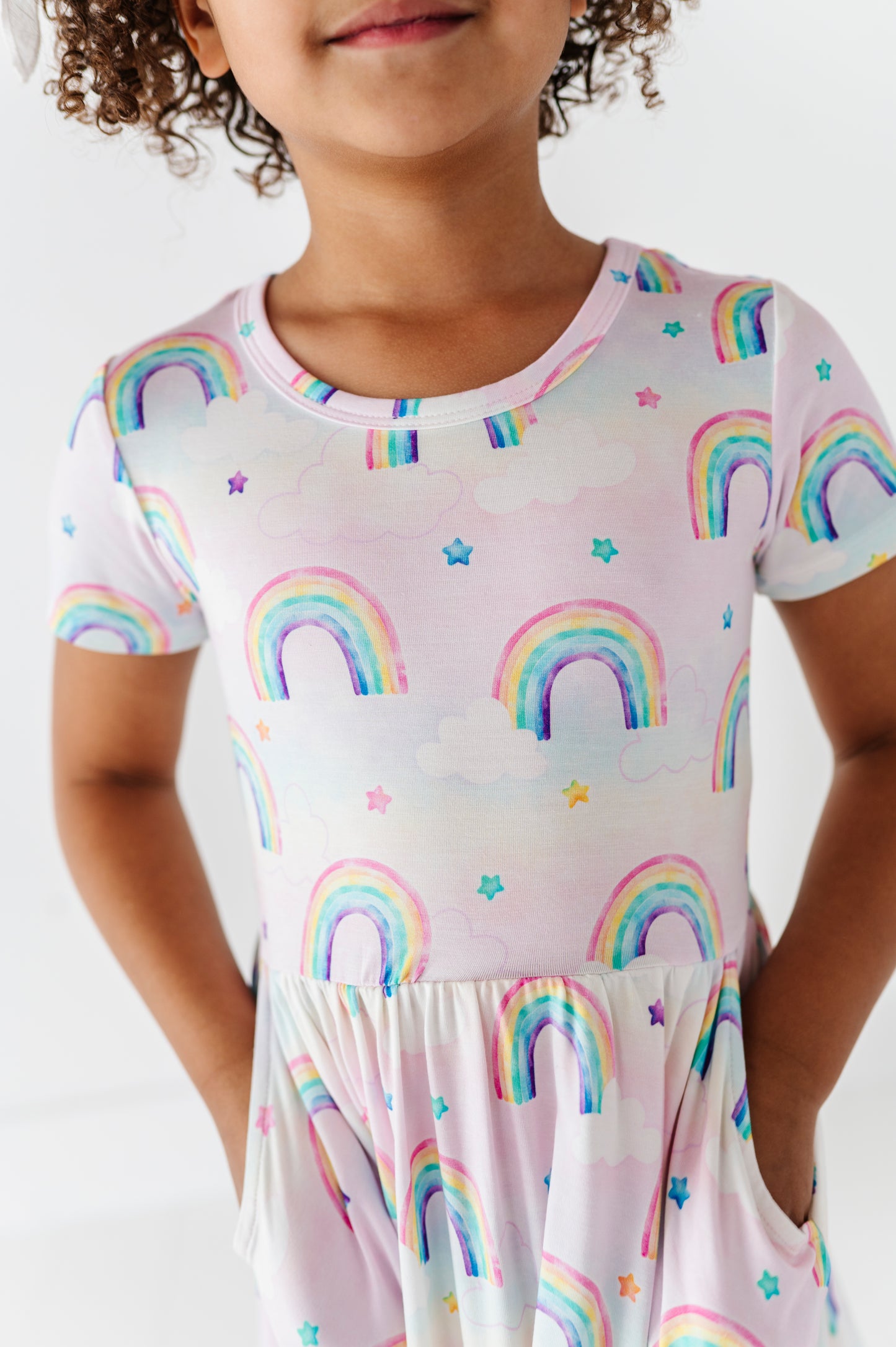 Child wearing a bamboo dress with watercolor rainbow pattern on a plain background