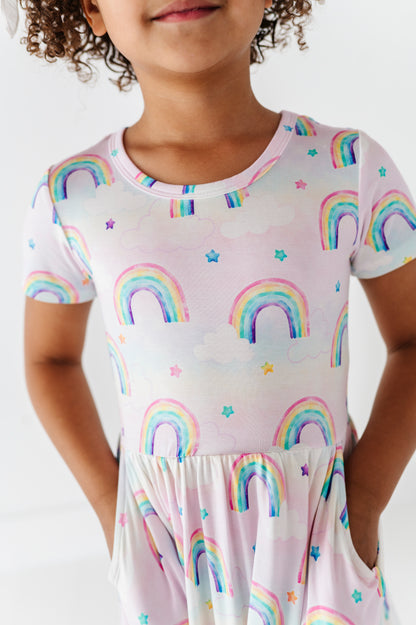 Child wearing a bamboo dress with watercolor rainbow pattern on a plain background