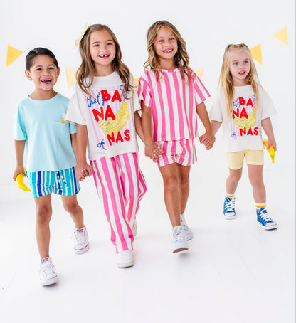 Four children modeling matching white graphic T-shirts with colorful 'Not A Banana' designs, paired with striped shorts or solid shorts, against a clean white studio background with yellow bunting.