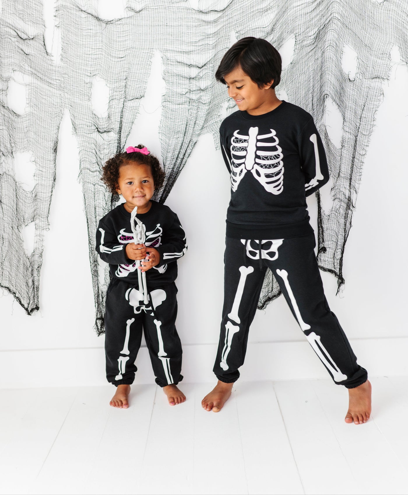 Two children wearing skeleton-themed outfits standing in front of a spider web backdrop.