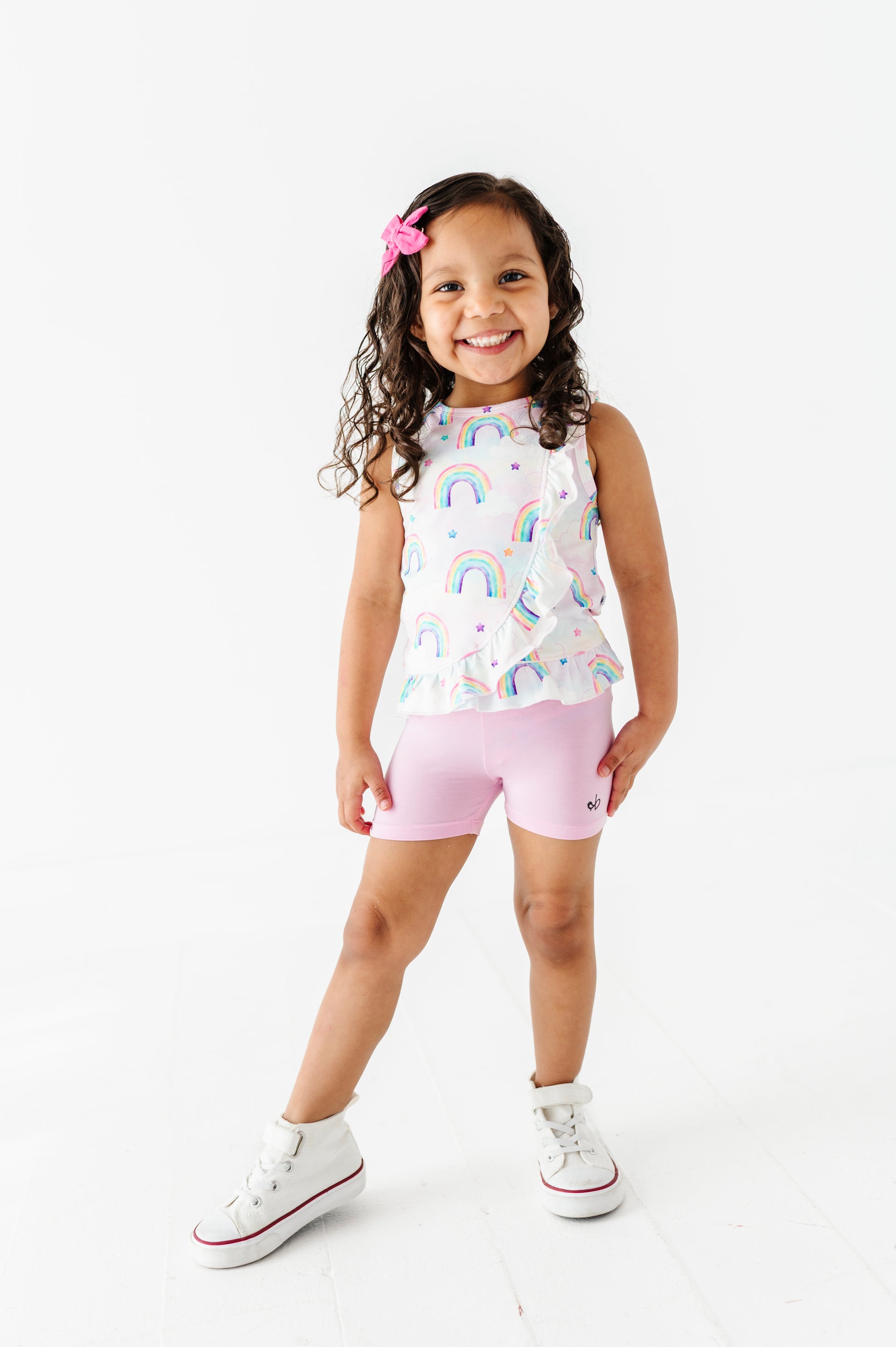Young girl wearing a bamboo cotton watercolor rainbow-patterned peplum top and bamboo biker pink shorts on a white background