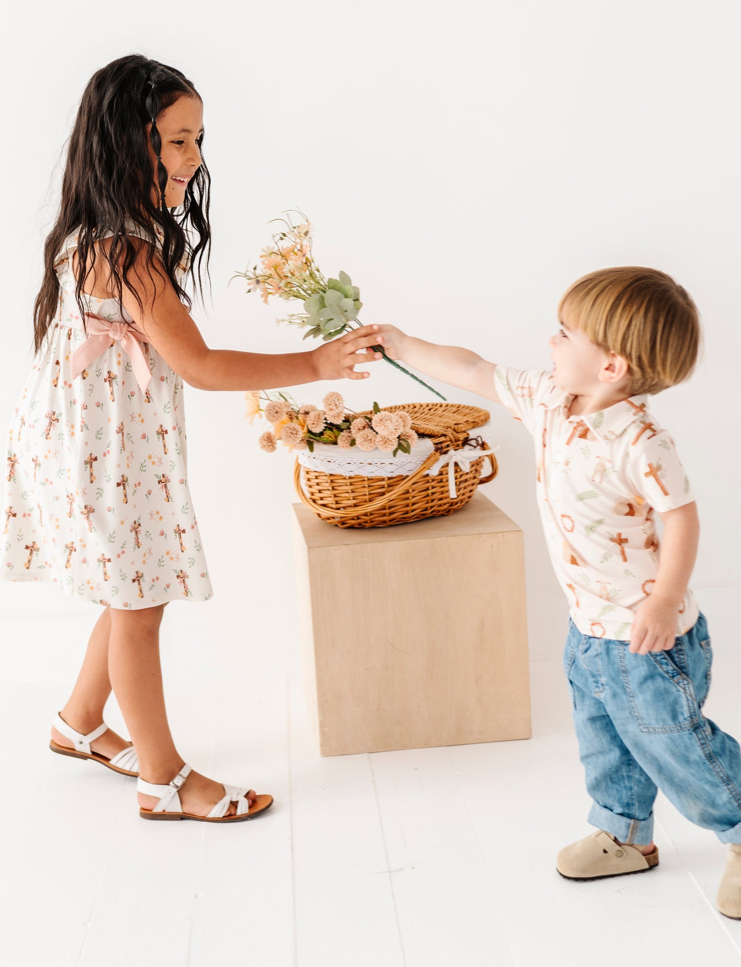 Two children exchanging flowers on a white background, while wearing Christian-themed Easter daywear