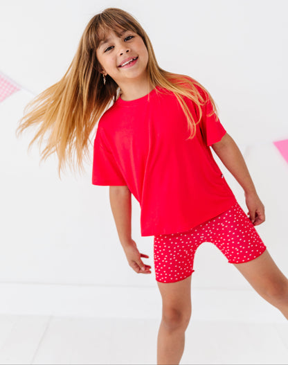 Young girl wearing a red shirt and red shorts with white polka dots on a white background