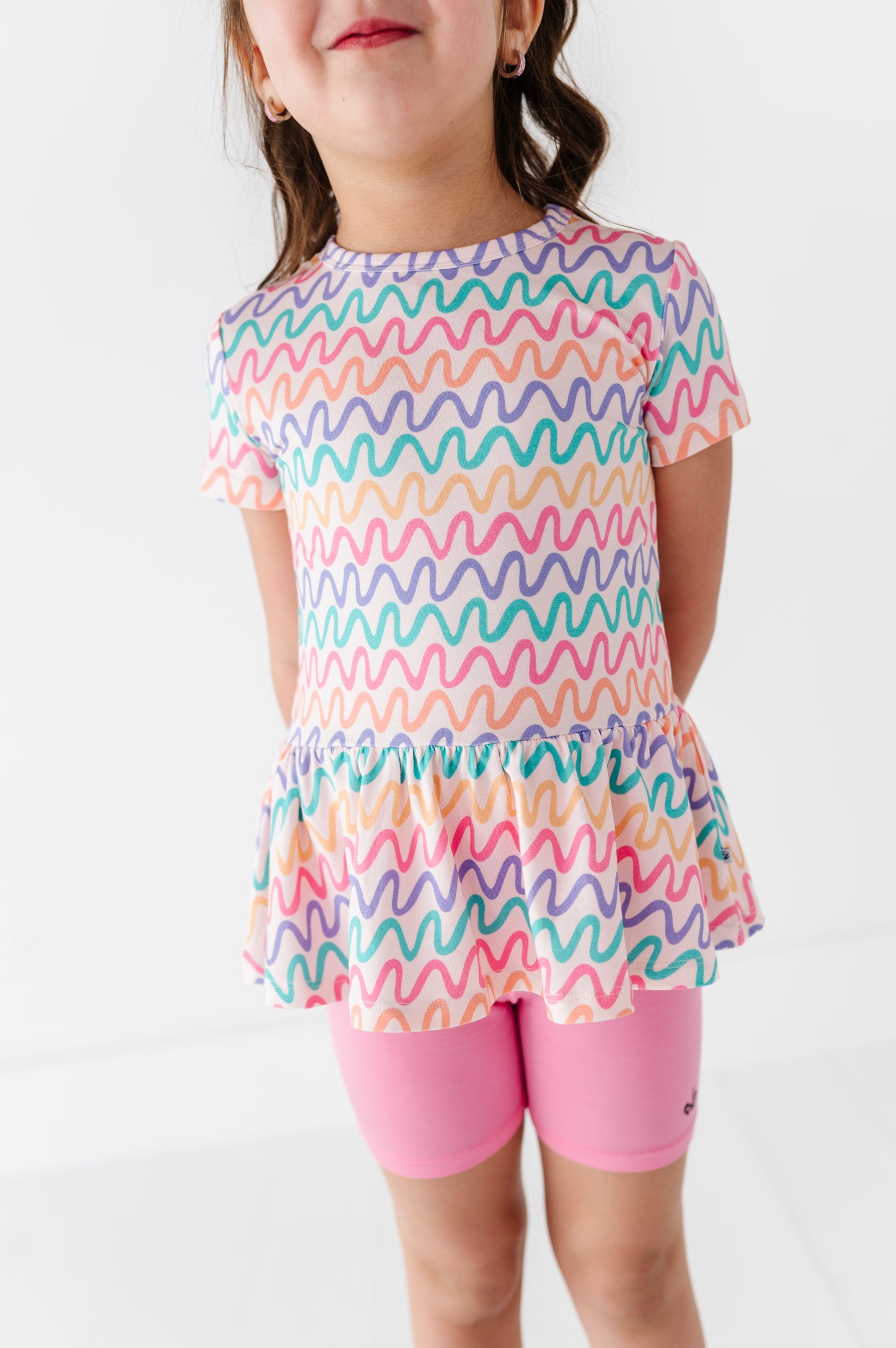 Child wearing a colorful wavy patterned bamboo/cotton top and pink bamboo biker shorts on a white background
