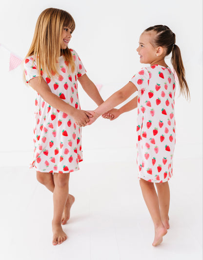 Two children wearing strawberry-patterned nightgowns on a white background