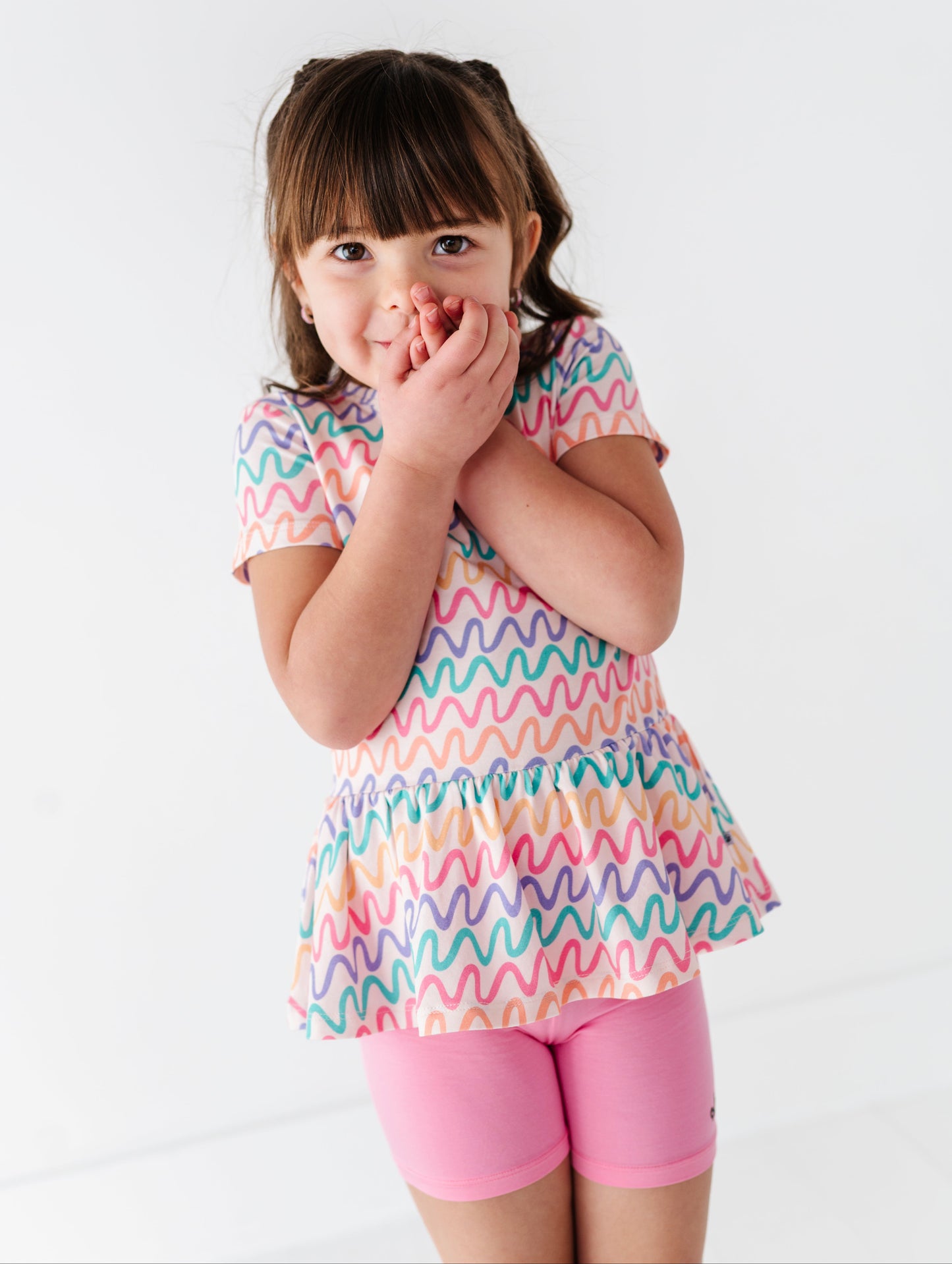 Young girl wearing a colorful wavy patterned bamboo/cotton top and pink bamboo biker shorts on a white background