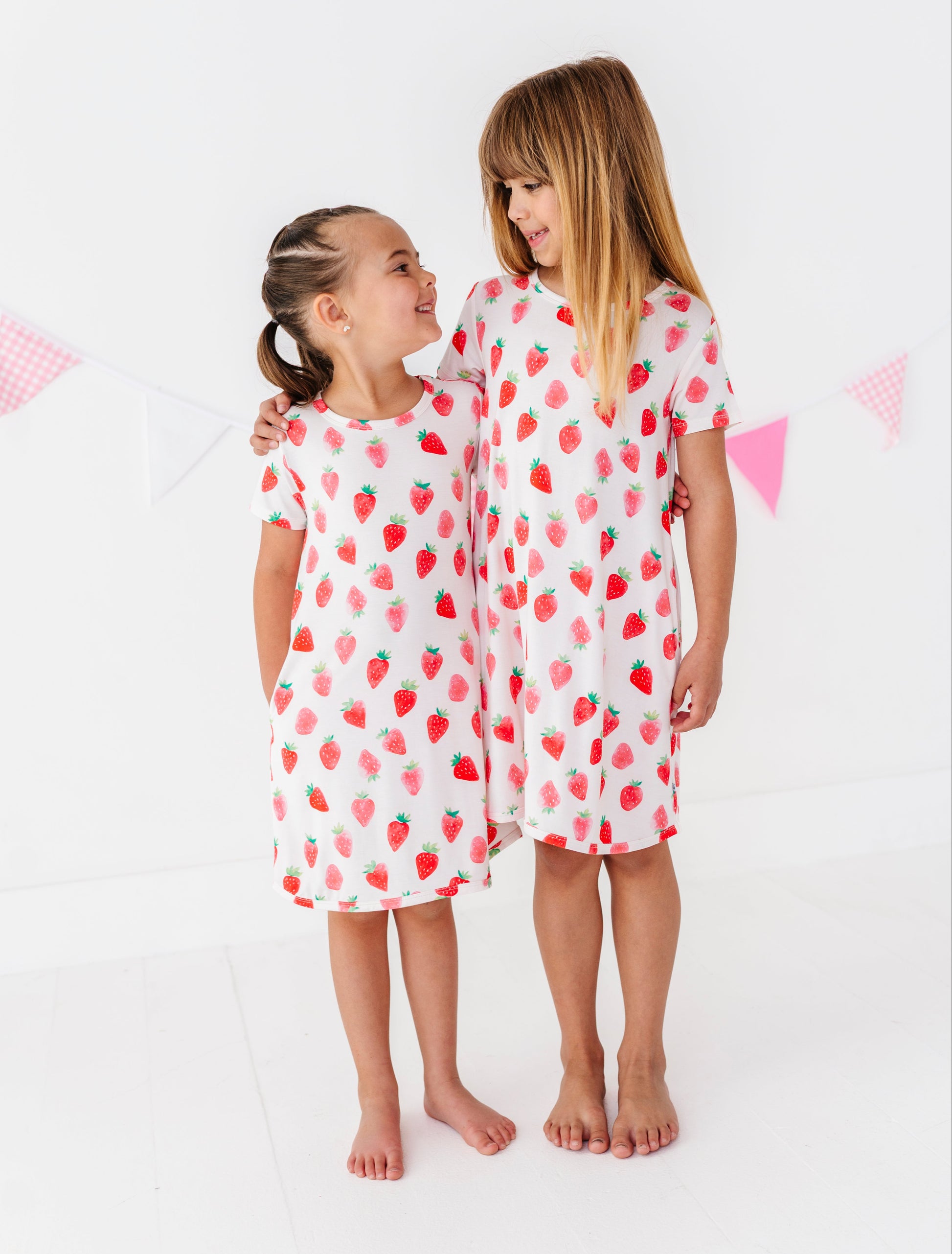 Two children wearing strawberry-patterned dresses  on a white background