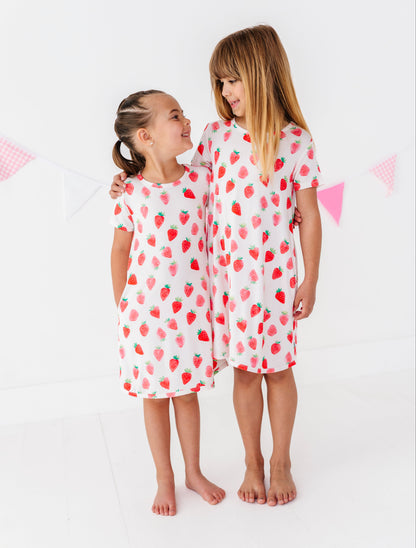 Two children wearing strawberry-patterned dresses  on a white background