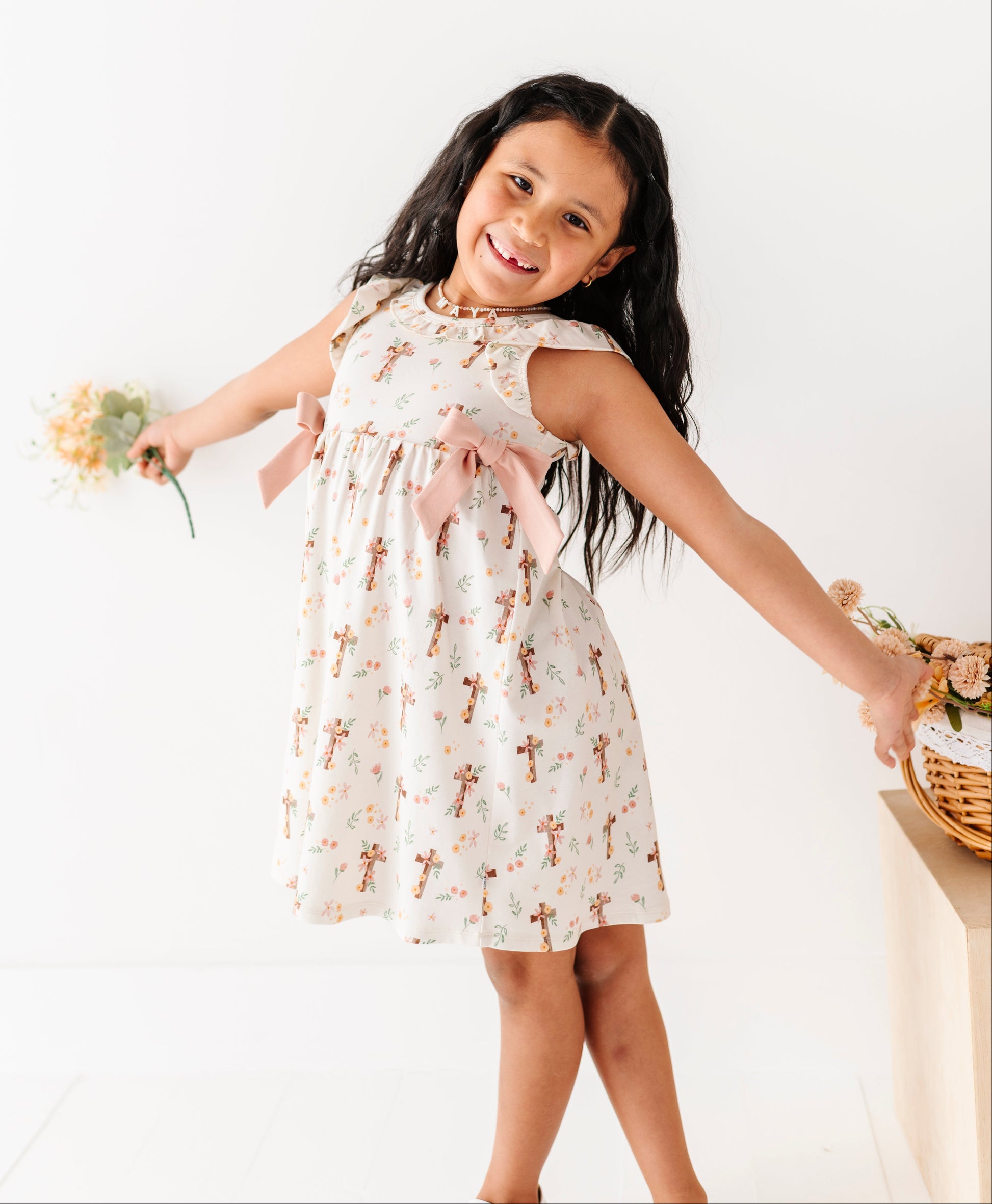 Young girl in a floral Easter dress holding flowers against a white background