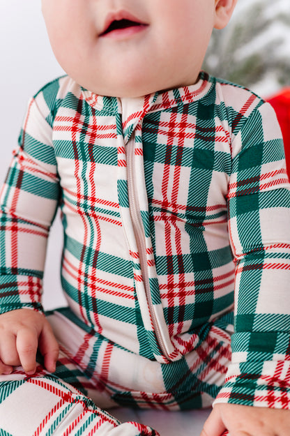 A close-up of a baby wearing a festive zip-up bamboo sleeper with a green, red, and white plaid pattern.