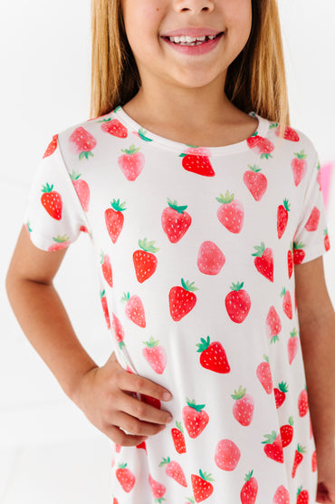 Child wearing a white dress with red strawberry pattern on a white background