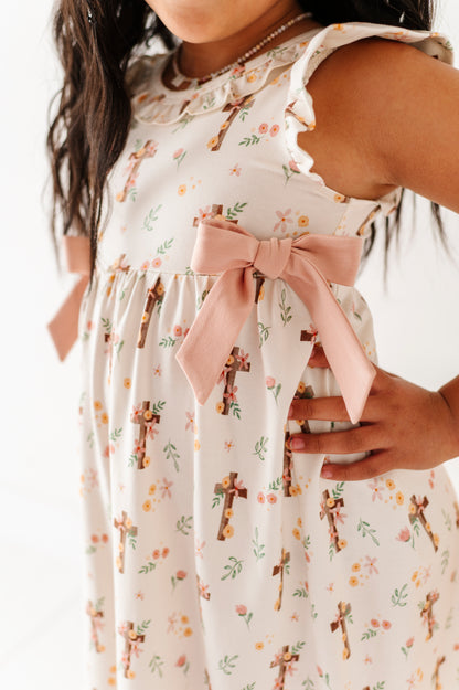 Little girl wearing a bamboo Easter dress featuring crosses, florals, and bows in a traditional Easter theme