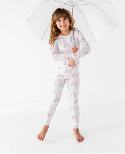 Child wearing a rainbow-patterned bamboo pajama set holding a clear umbrella on a white background