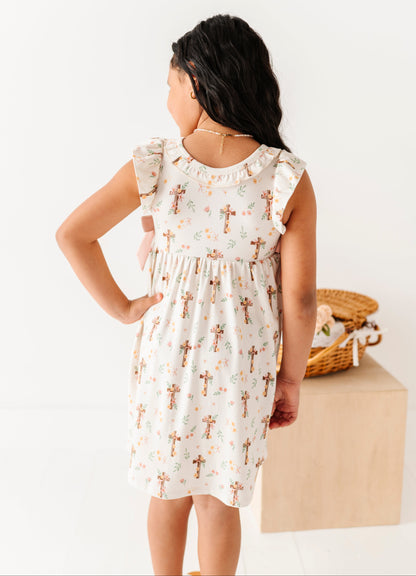 Young girl wearing a white bamboo dress with a floral pattern, standing against a plain background.