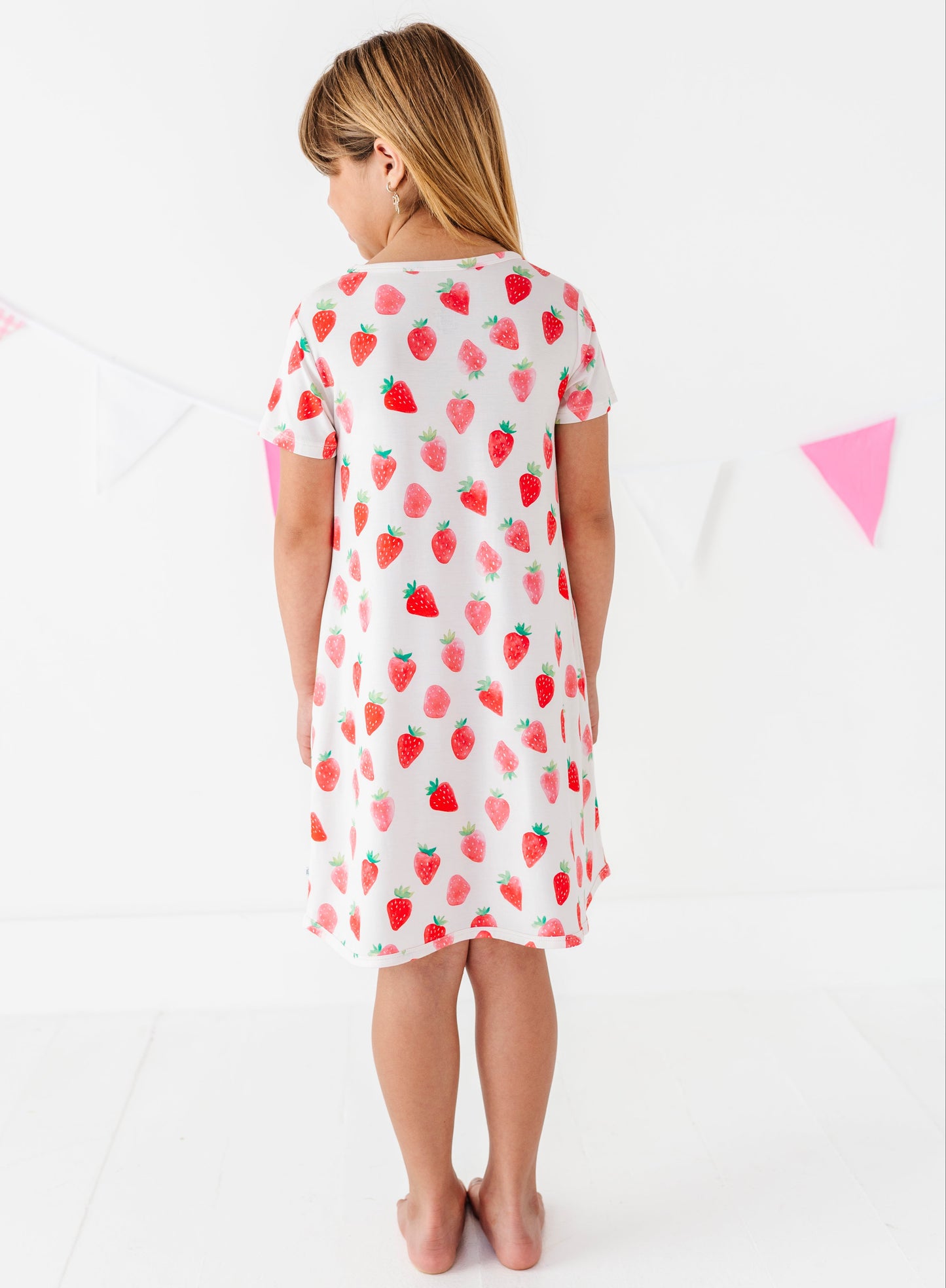 Child wearing a white dress with red strawberry pattern on a white background
