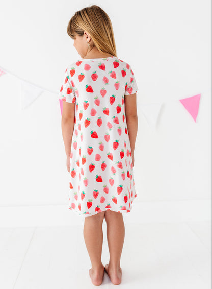 Child wearing a white dress with red strawberry pattern on a white background