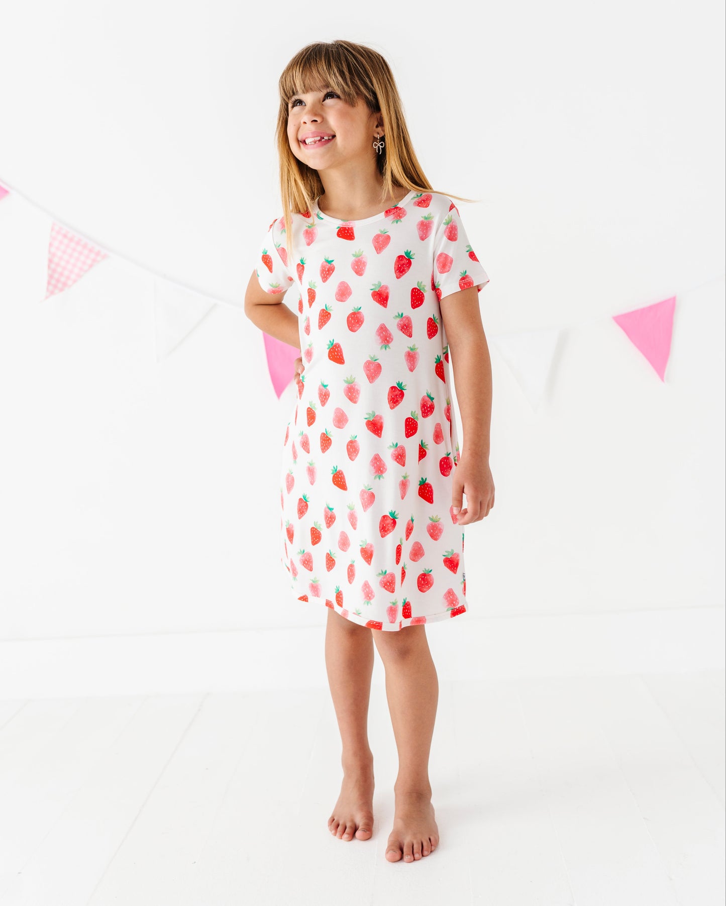 Young girl wearing a white dress with red strawberry patterns on a white background