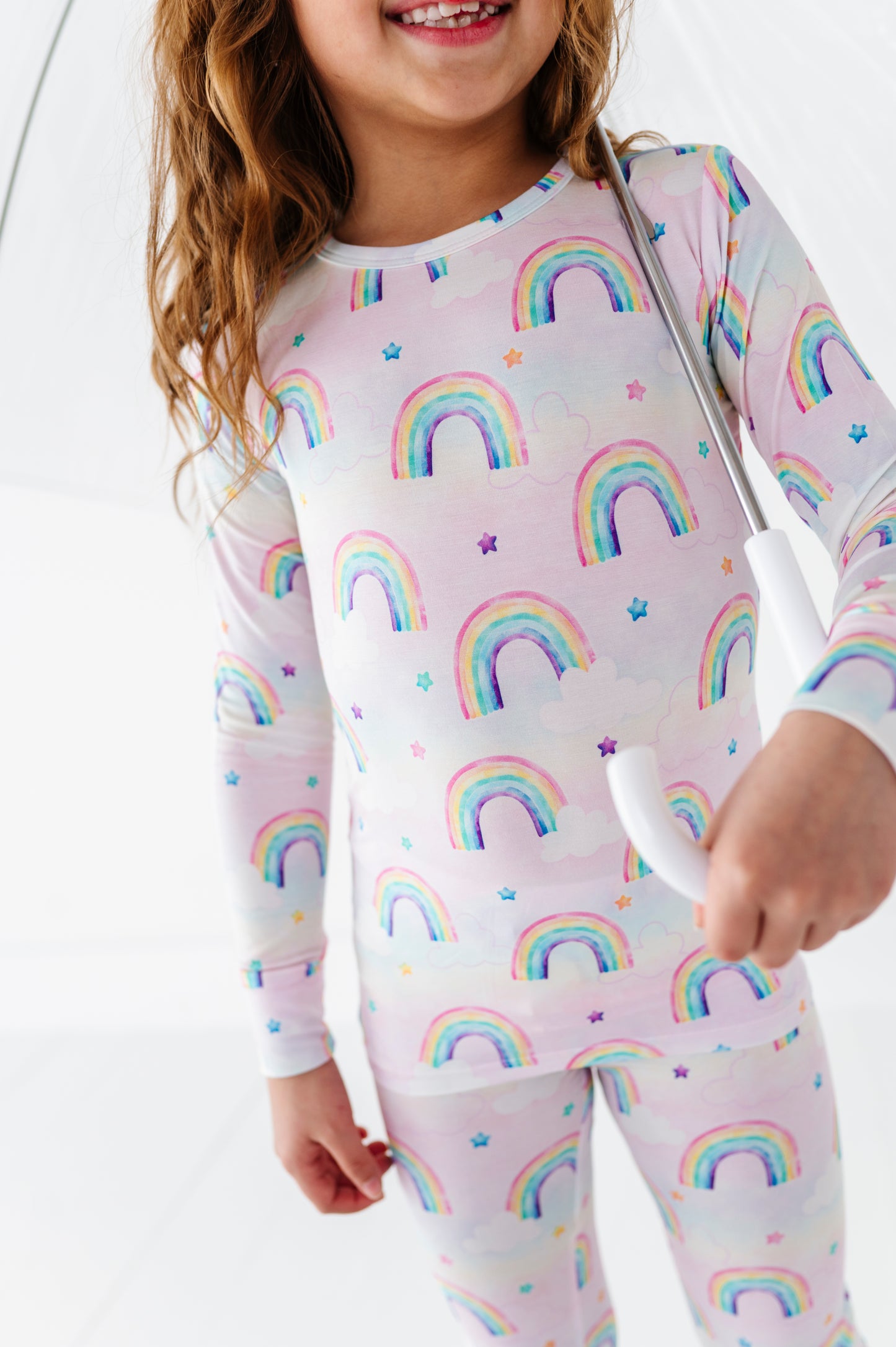 Child wearing a bamboo two-piece pajama set with watercolor rainbow pattern on a white background