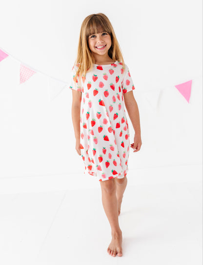 Young girl wearing a white dress with red strawberry pattern on a white background