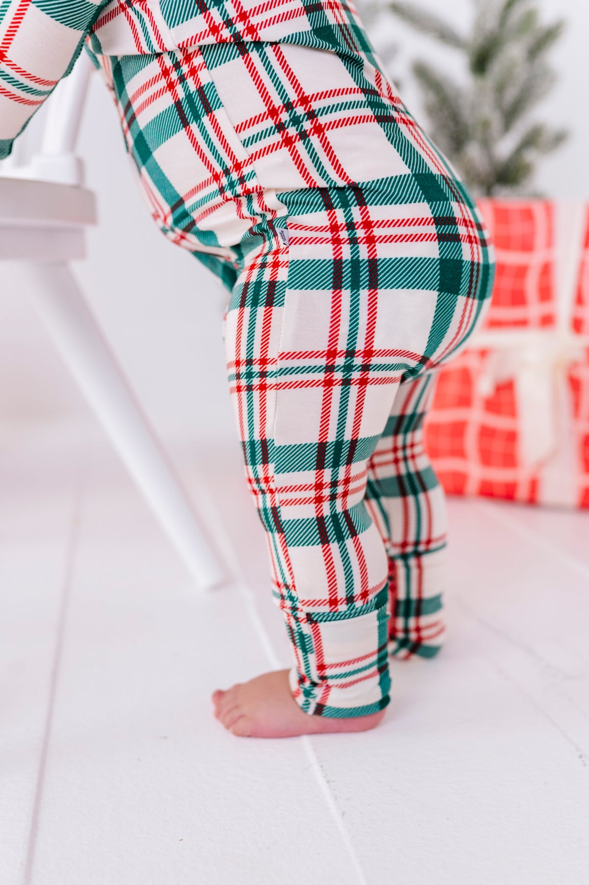 The side view of a baby wearing a red, green, and beige convertible romper. It's a stretchy, durable, super soft bamboo zip romper 