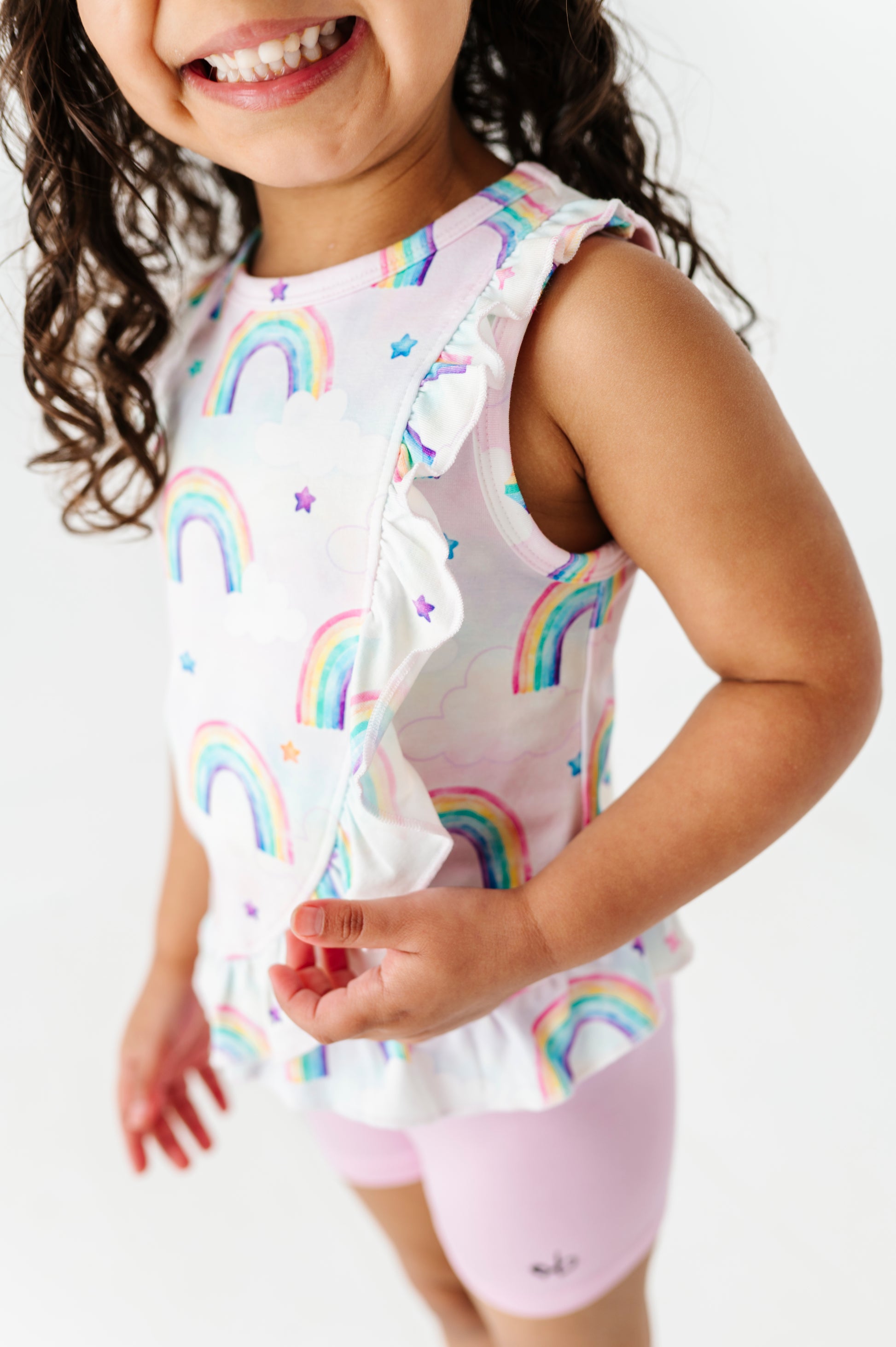 Child wearing a white sleeveless bamboo cotton peplum top with watercolor rainbow patterns and pink bamboo biker shorts on a white background