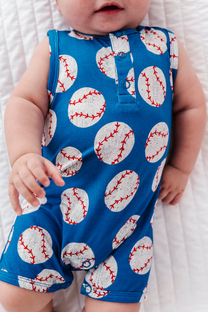 Baby wearing a blue romper with baseball pattern on a white blanket