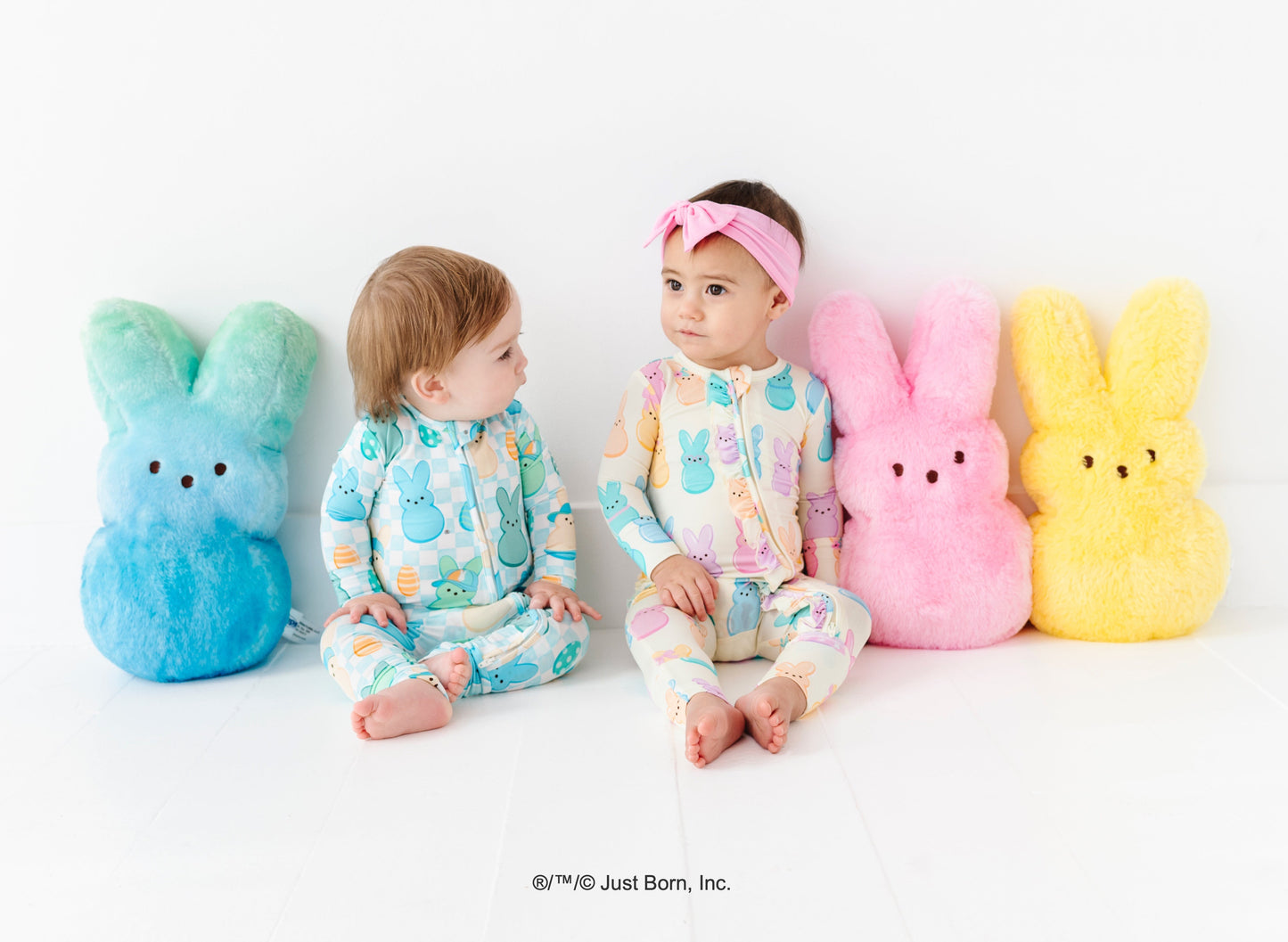 Two children in pajamas sitting between colorful Peeps plush toys on a white background