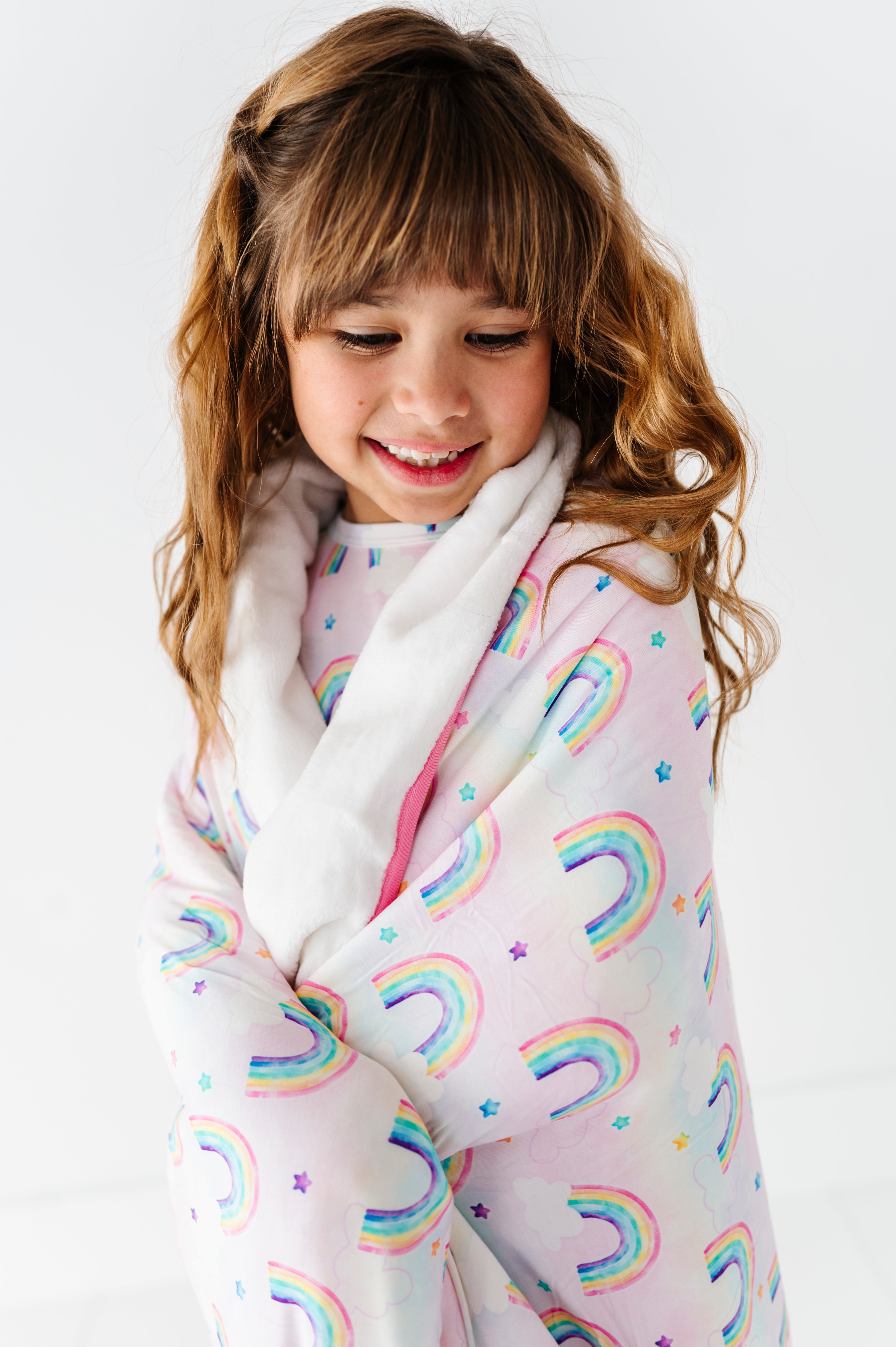 Little girl wrapped in a bamboo plush blanket featuring watercolor rainbows 