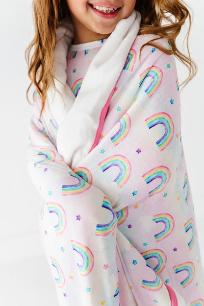 Child wearing a bamboo plush blanket with watercolor rainbow patterns on a plain background
