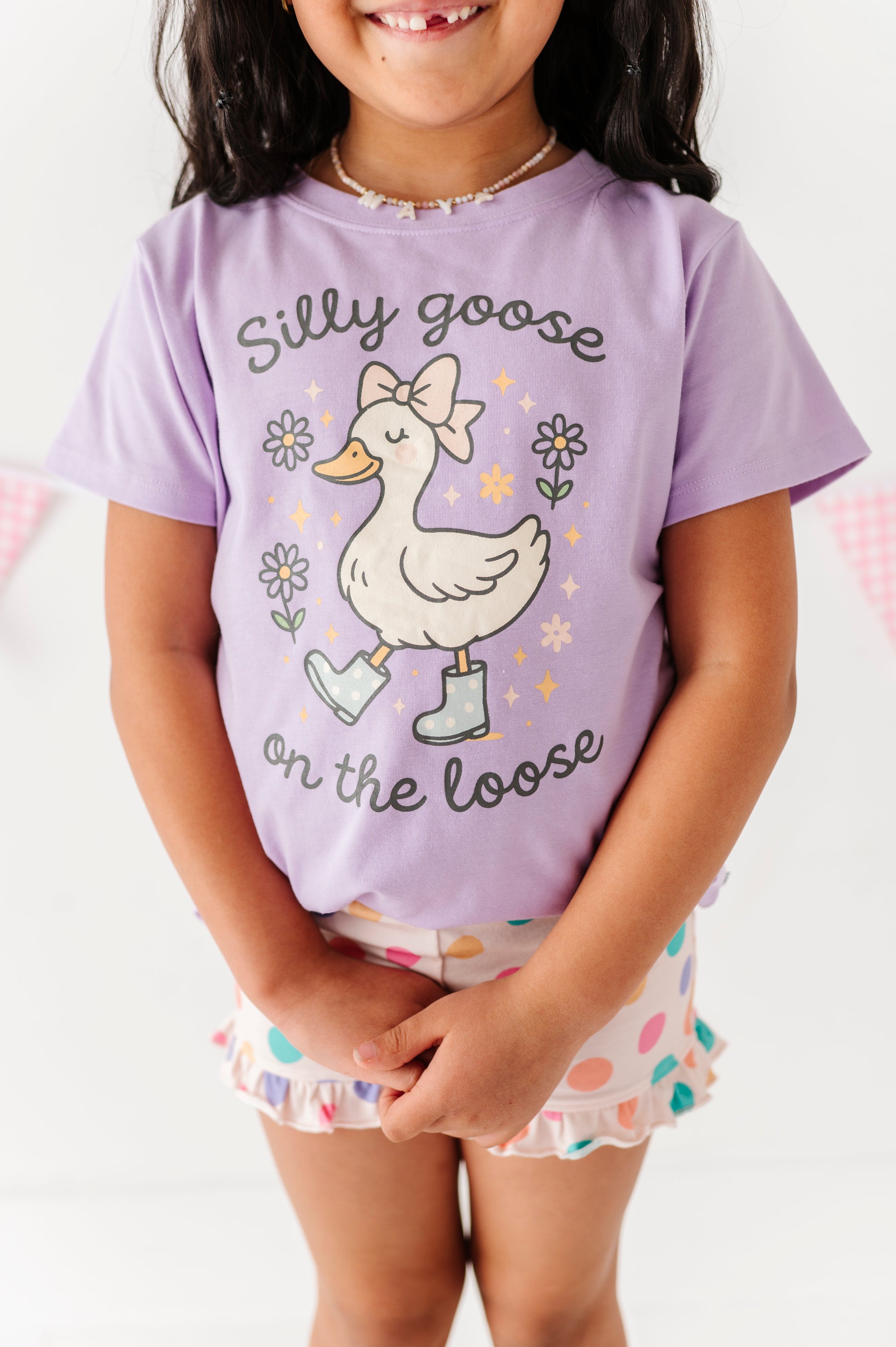 Child wearing a purple t-shirt with a goose graphic and text, standing against a white background.