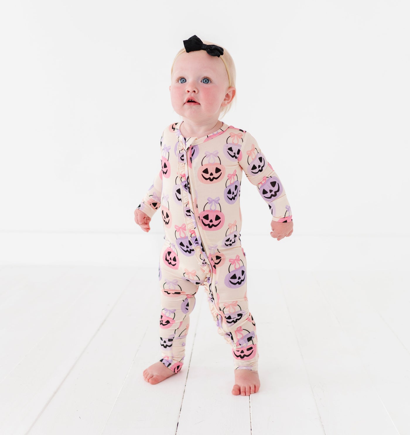 Baby wearing a onesie with pumpkins and ghosts on a white background