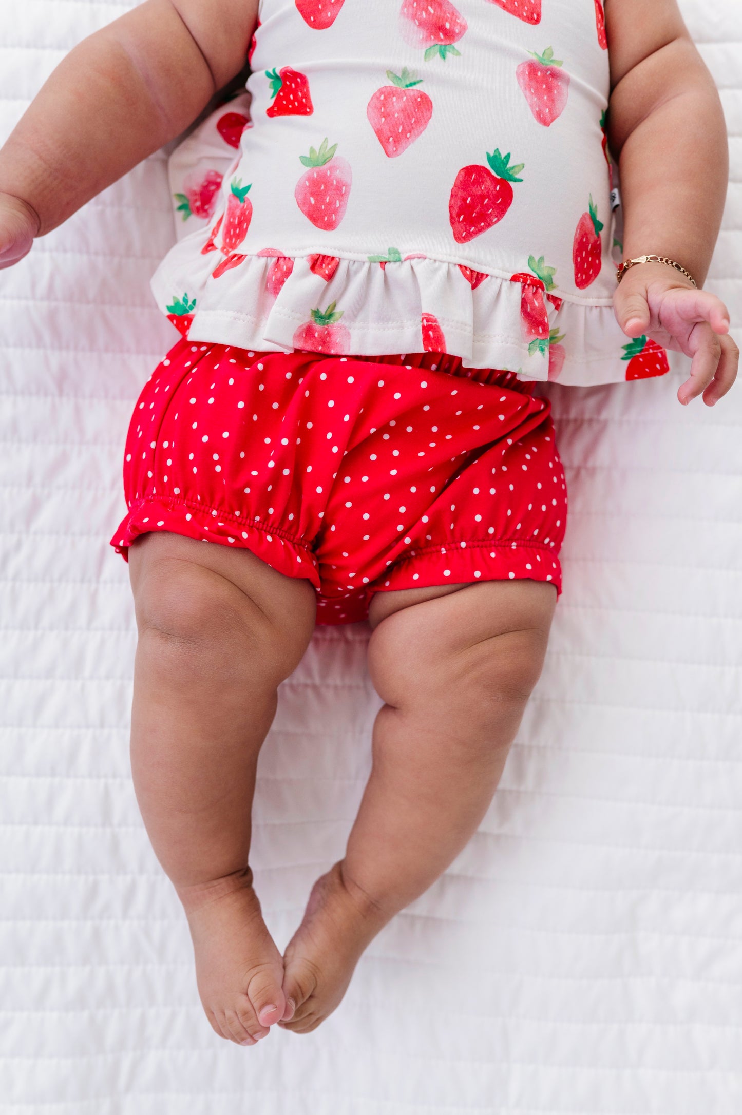 Baby wearing a strawberry-patterned top and red bloomers on a white background